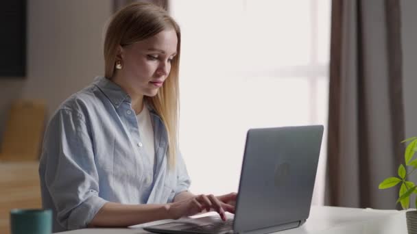 Mobilne biuro w domu. Młoda kobieta siedząca w kuchni w domu, pracująca na laptopie. Styl życia dziewczyna studiuje lub pracuje w pomieszczeniach. Koncepcja kwarantanny prowadzenia działalności na własny rachunek — Wideo stockowe