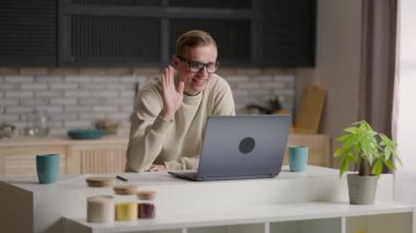 Gülümseyen genç erkek canlı yayında bilgisayar ve video konferans kullanarak iletişim kuruyor. Genç erkek video bağlantısıyla iletişim kurarken not alıyor