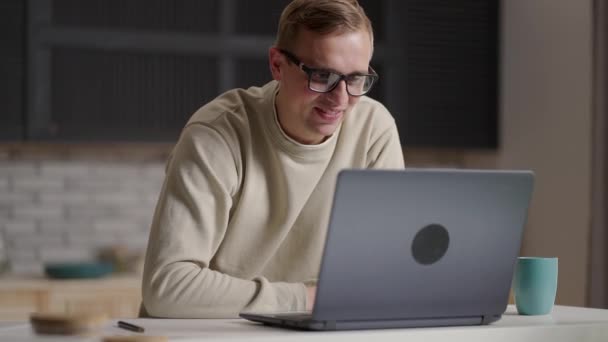 Gülümseyen genç erkek canlı yayında bilgisayar ve video konferans kullanarak iletişim kuruyor. Genç erkek video bağlantısıyla iletişim kurarken not alıyor — Stok video
