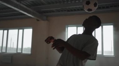 Zenci futbolcu futbolcu, içi boş bir otoparkta top oynarken, tekmeler ve hareketler yapıyor. Afrikalı çocuk Urban City 'de serbest stil eğitimi alıyor. Yavaş çekim RAW derecelendirilmiş görüntüler