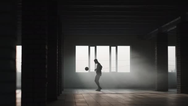 Un hombre negro hace un estilo libre de fútbol con una pelota en un estacionamiento subterráneo a la luz del sol. Disparos en cámara lenta hacer malabares con la pelota en el estacionamiento subterráneo. — Vídeos de Stock