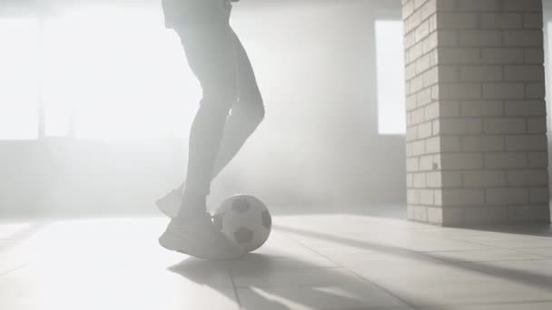 Fútbol de primer plano goteando en cámara lenta en un estacionamiento subterráneo a la luz del sol. Corre con la pelota en un entorno urbano. Entrenamiento de un niño soñando con convertirse en futbolista — Vídeo de stock