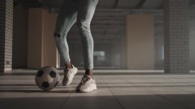 Afro-Amerikan futbolcu boş kapalı otoparkta tekme pratiği yapıyor ve hareket ediyor. Ağır çekimde siyah adam güneş ışığında yeraltı parkında top sürerek antrenman yapıyor..