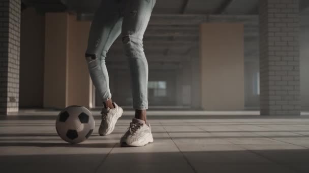 Jugador de fútbol afroamericano practicando patadas y se mueve dentro de estacionamiento cubierto vacío. El hombre negro de cámara lenta resuelve el fútbol goteando en el parque subterráneo a la luz del sol. — Vídeos de Stock