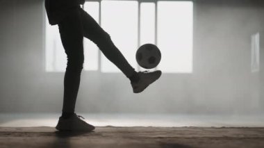 Yakın plan siyahi bir adam garajda güneş ışığında futbol topuyla hokkabazlık yapıyor. Şehir ortamında gün batımında serbest futbol. Toz ve gün batımı