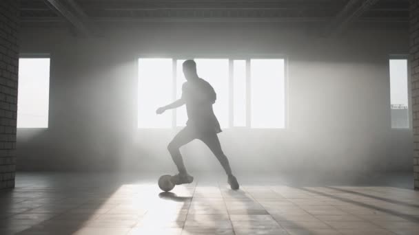 Черный человек делает футбольный фристайл с мячом на подземной парковке под солнцем. Медленная стрельба жонглирует мячом на подземной парковке. — стоковое видео
