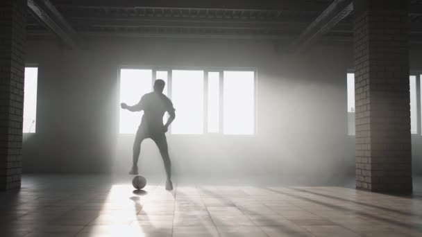 Giocatore di calcio afro-americano che pratica calci e si muove all'interno del garage coperto vuoto. rallentatore nero uomo lavorare fuori calcio dribbling in sotterraneo parkin in luce solare. — Video Stock
