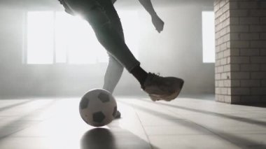 Afro-Amerikan futbolcu boş kapalı otoparkta tekme pratiği yapıyor ve hareket ediyor. Ağır çekimde siyah adam güneş ışığında yeraltı parkında top sürerek antrenman yapıyor..