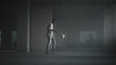 Siyah bir adam, güneş ışığında bir yeraltı otoparkında topla serbest bir futbol topu yapıyor. Ağır çekim yeraltı otoparkında topu hokkabazlık yapıyor.. 