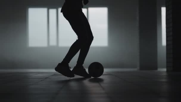 A silhueta de um jogador de futebol treinando em um estacionamento subterrâneo ao sol e poeira nascente. O conceito do sucesso das aspirações desportivas e da perseverança. Futebol livre — Vídeo de Stock