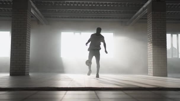 Замедление футбольного фристайла. Молодой черный мужчина тренируется с футбольным мячом на подземной парковке. Тренерство молодого афроамериканца, стремящегося стать футболистом и работающего над своей мечтой — стоковое видео