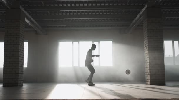 Un uomo nero fa un freestyle di calcio con una palla in un parcheggio sotterraneo alla luce del sole. Lento-motion tiro giocoliere la palla nel parcheggio sotterraneo. — Video Stock
