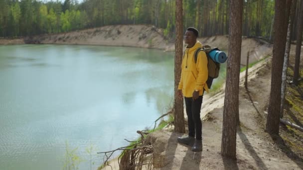 Bagsidebillede af en sort mand, der kigger på bjerg og sø. Langsom bevægelse – Stock-video
