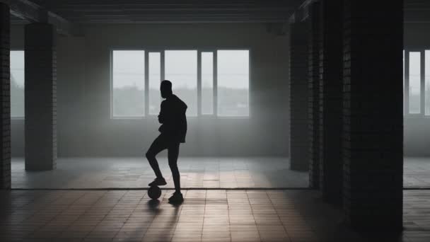 La silhouette di un giocatore di calcio che si allena in un parcheggio sotterraneo al sole e la polvere che sorge. Il concetto del successo delle aspirazioni sportive e della perseveranza. Freestyle calcio — Video Stock