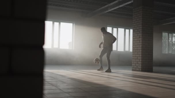 Черный человек делает футбольный фристайл с мячом на подземной парковке под солнцем. Медленная стрельба жонглирует мячом на подземной парковке. — стоковое видео