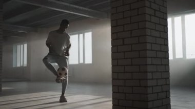 Siyah bir adam, güneş ışığında bir yeraltı otoparkında topla serbest bir futbol topu yapıyor. Ağır çekim yeraltı otoparkında topu hokkabazlık yapıyor.. 