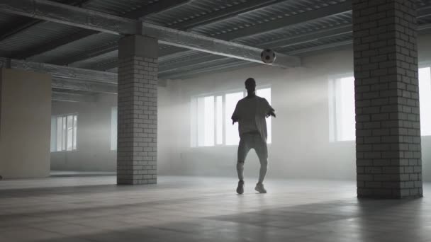 Un negro entrena con una pelota de fútbol en un estacionamiento subterráneo a la luz del sol en cámara lenta. Haz malabares con la pelota y entrena el pase y patea. Trabajo sobre el éxito — Vídeos de Stock