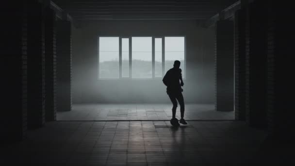 La silueta de un jugador de fútbol entrenando en un estacionamiento subterráneo bajo el sol y el polvo naciente. El concepto del éxito de las aspiraciones deportivas y la perseverancia. Fútbol estilo libre — Vídeo de stock