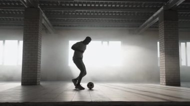 Genç siyahi bir adam yeraltı otoparkında ağır çekimde futbol oynuyor. Koş ve topu sür.