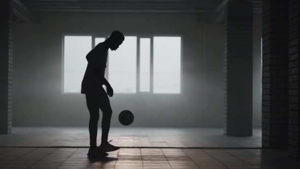 Un hombre negro hace un estilo libre de fútbol con una pelota en un estacionamiento subterráneo a la luz del sol. Disparos en cámara lenta hacer malabares con la pelota en el estacionamiento subterráneo. — Vídeo de stock