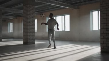 Siyah bir adam, güneş ışığında bir yeraltı otoparkında topla serbest bir futbol topu yapıyor. Ağır çekim yeraltı otoparkında topu hokkabazlık yapıyor.. 