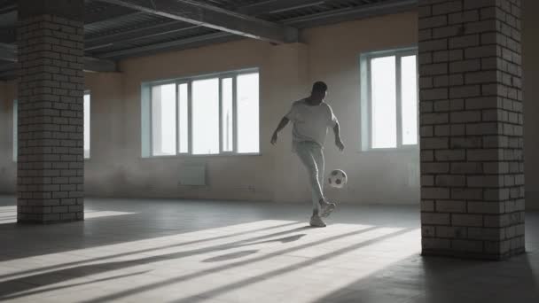 Homem negro jogador de futebol praticando truques, chutes e movimentos com bola dentro vazio garagem coberta. Rapaz africano treinando estilo livre na cidade urbana. Filmagem RAW em câmera lenta graduada — Vídeo de Stock