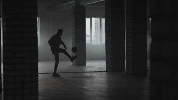 Een man schopt de voetbal tegen een muur op een ondergrondse parkeerplaats in het zonlicht in slow motion — Stockvideo