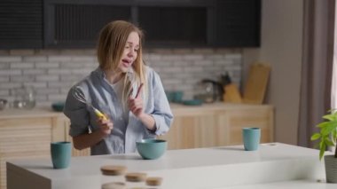 Sabahın erken saatlerinde mutfakta dans eden çekici kız. Sabahın erken saatlerinde mutfakta genç bir kadın. Gömlekli kız kahvaltı hazırlayacak.