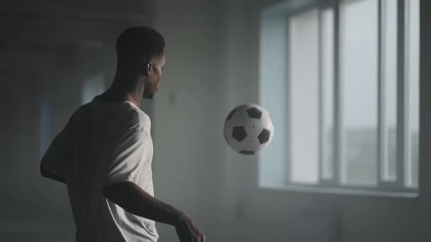 Een man schopt de voetbal tegen een muur op een ondergrondse parkeerplaats in het zonlicht in slow motion — Stockvideo