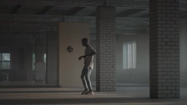 Esmer tenli bir genç otoparkta futbol antrenmanı yapıyor. Futbol serbest stili. Ağır çekimde hokkabazlık.