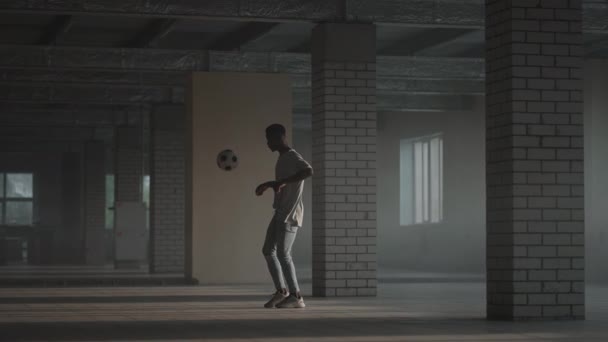 Темнокожий подросток проводит футбольную тренировку на наземной парковке. Футбольный фристайл. Мяч для жонглирования медленным движением — стоковое видео
