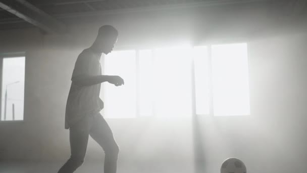 Černoch fotbalista trénuje triky, kopy a pohyby s míčem uvnitř prázdné kryté garáže. Zpomalit městský životní styl města — Stock video