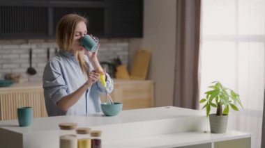 Sabahın erken saatlerinde mutfakta dans eden çekici kız. Sabahın erken saatlerinde mutfakta genç bir kadın. Gömlekli kız kahvaltı hazırlayacak.