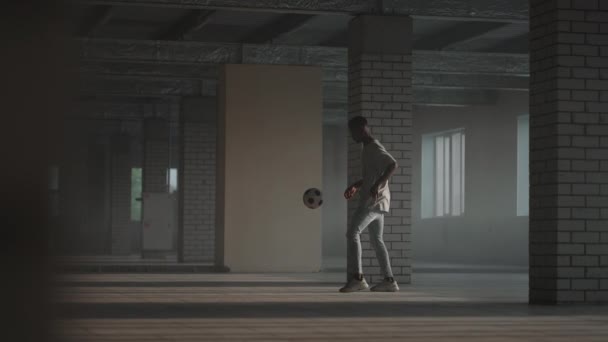 Svart pojke fotboll fotbollsspelare öva tricks, sparkar och flyttar med bollen inuti tomma täckta parkeringshus. Slow motion Stadsliv — Stockvideo