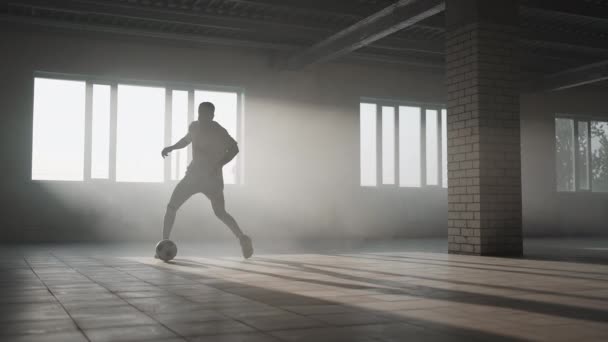 Jugador de fútbol afroamericano practicando patadas y se mueve dentro de estacionamiento cubierto vacío. El hombre negro de cámara lenta resuelve el fútbol goteando en el parque subterráneo a la luz del sol. — Vídeos de Stock