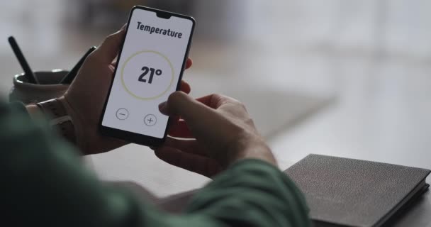 L'uomo sta controllando il sistema di smart home utilizzando l'app nel cellulare, regolando la temperatura nella stanza e accendendo il sistema di sicurezza, vista da vicino — Video Stock