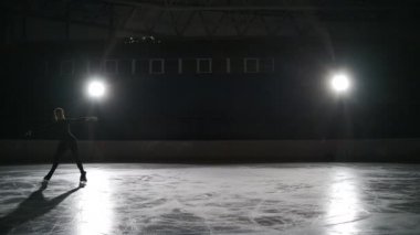 Kapalı alandaki buz patencileri karanlıkta spot ışıklarıyla antrenman yapıyor. Stadyumda tek kişilik buz pateni. Kız artistik patinaj yapıyor, kartal gibi yayılıyor.