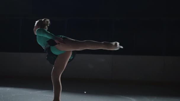 Medium shot in slow motion, een jonge sportvrouw bereidt zich voor om te concurreren in een jurk de avond ervoor. Meisje voert een basiselement van kunstschaatsen rotatie staande op een been slikken — Stockvideo