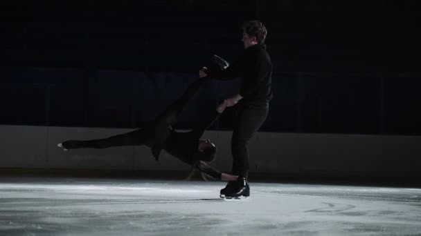 En cámara lenta: una joven pareja de patinadores artísticos está realizando una coreografía de patinaje en pista de hielo antes de comenzar una competición. Concepto de perfección, precisión, libertad, pasión — Vídeo de stock