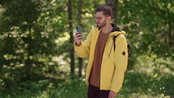 Man wandelaar met behulp van smartphone tijdens het weekend in het bos. Low angle view van aantrekkelijke man backpacker planning reis route in het bos op mobiele telefoon — Stockvideo
