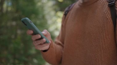 Ormanda yürüyen bir erkek gezginin elindeki cep telefonunun yakın çekimi. Sosyal ağlar seyir subayı ve ulak. Ormanda yürümek için cep telefonunu kullan.