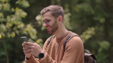 Bir adam ormanda yürüyor ve cep telefonuna bir mesaj yazıyor. Sırt çantalı bir turist yürüyüş sırasında telefonuna bir mesaj basıyor.