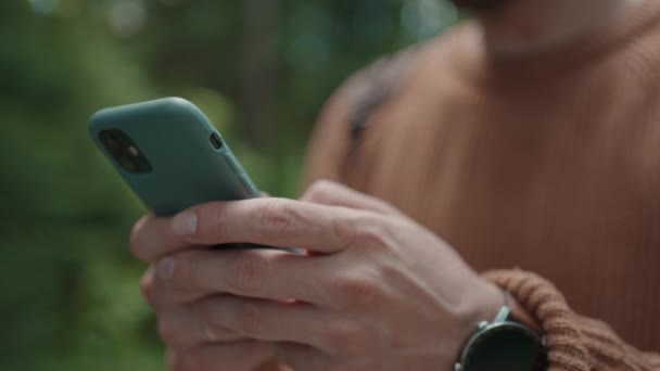 Ein Mann geht im Wald spazieren und schreibt eine Nachricht auf sein Handy. Tourist mit Rucksack druckt auf einer Wanderung eine Nachricht in sein Handy — Stockvideo