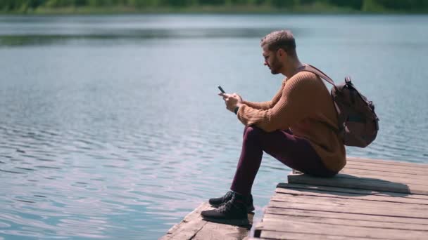 スローモーションで木製の湖の桟橋に座って携帯電話に道を開くメッセージを印刷します。 — ストック動画