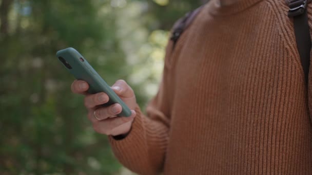 Närbild av en mobiltelefon i händerna på en manlig resenär som går genom skogen. Sociala nätverk Navigatör och budbärare. Använd din mobiltelefon för en promenad i skogen — Stockvideo