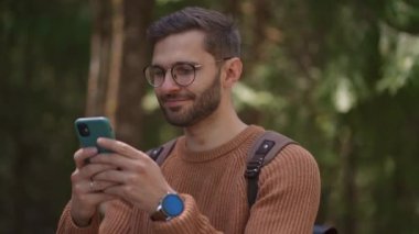 Bir adam ormanda yürüyor ve cep telefonuna bir mesaj yazıyor. Sırt çantalı bir turist yürüyüş sırasında telefonuna bir mesaj basıyor.