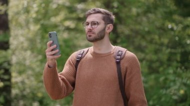 Yürüyüşçü, hafta sonları ormanda eğlenirken akıllı telefon kullanıyor. Ormanda cep telefonuyla seyahat rotası planlayan çekici bir adamın düşük açılı görüntüsü.