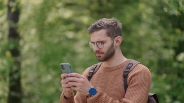 Yürüyüşçü, hafta sonları ormanda eğlenirken akıllı telefon kullanıyor. Ormanda cep telefonuyla seyahat rotası planlayan çekici bir adamın düşük açılı görüntüsü.