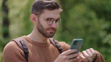 Sırt çantalı ve gözlüklü genç sakallı bir adam, GPS 'i ayarlamak ve ayarlamak için telefonunu kullanarak akıllı bir saati ayarlar. Modern teknoloji saatle yön buluyor. Etkinlik kontrolü