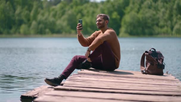 Хоробрий чоловік фотографує в лісовому озері зі смартфоном, фотографуючи мальовничий краєвид на фоні природи, насолоджуючись подорожами у відпустці. Повільний рух — стокове відео